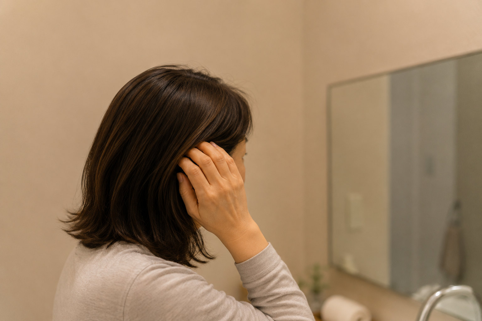 夜、鏡の前で髪の分け目を見る女性